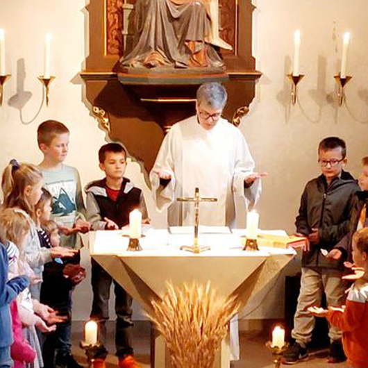 Am Altar der Kirche in Püssensheim steht die Gemeindereferentin. Um sie herum sind mehrere Kinder.